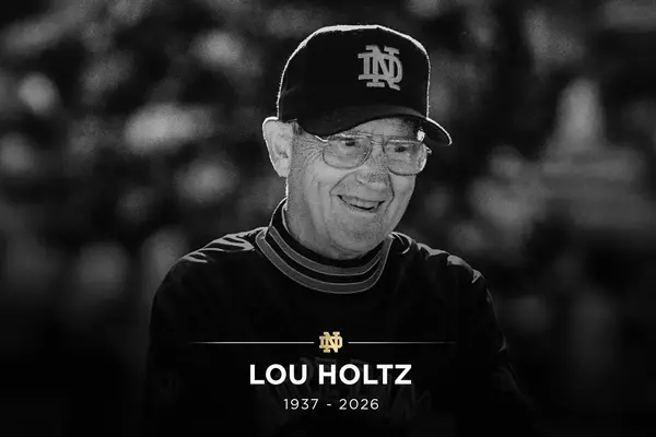 A smiling Lou Holtz in black and white, wearing a Notre Dame cap and glasses. Text: LOU HOLTZ, 1937 - 2026.