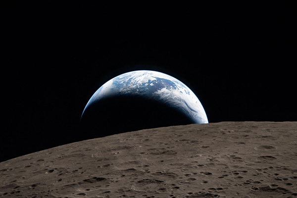 Earthset captured through the Orion spacecraft window during the Artemis II crew’s flyby of the Moon. A muted blue Earth with bright white clouds sets behind the cratered lunar surface.